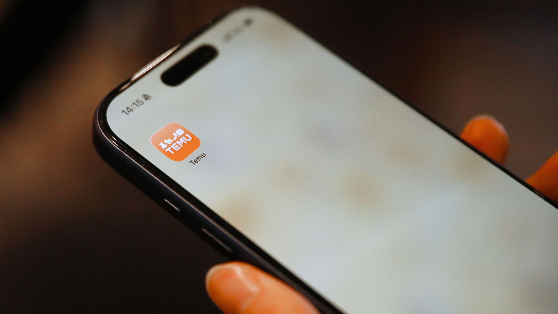 Hand holding smartphone with a shopping app icon visible, focusing on digital convenience.