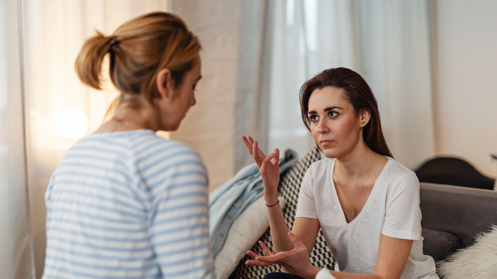 Two women sitting on a sofa, engaged in a serious discussion at home.