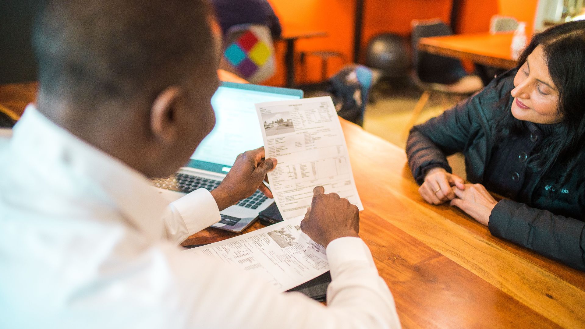 Two adults discussing documents in a business setting indoors.