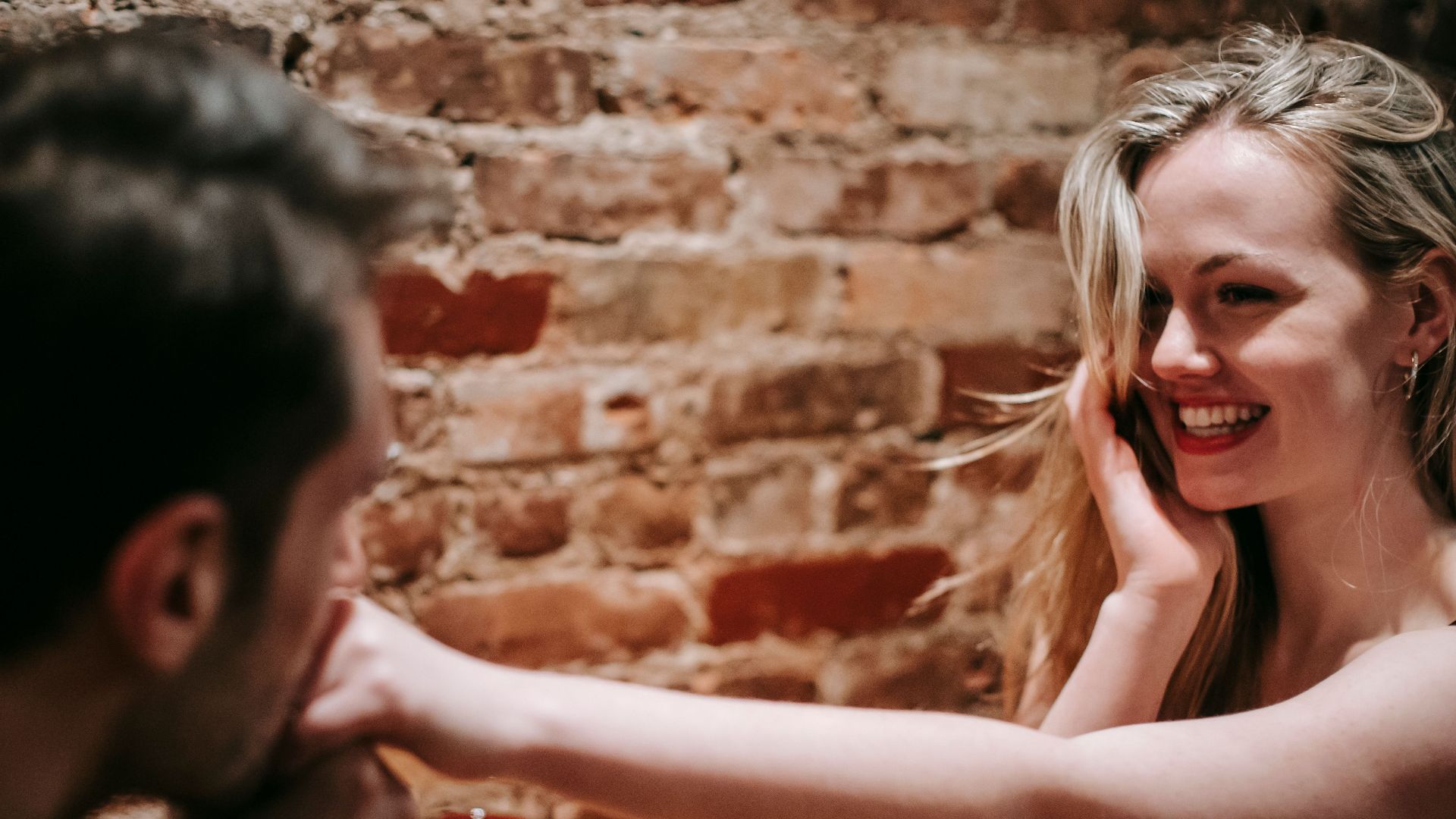 Unrecognizable young man kissing hand of young cheerful blond woman sitting at table in cafe