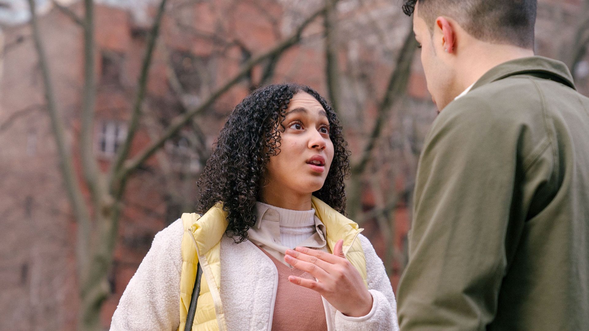 From below of ethnic female with short curly hair standing and arguing with boyfriend on street in daylight