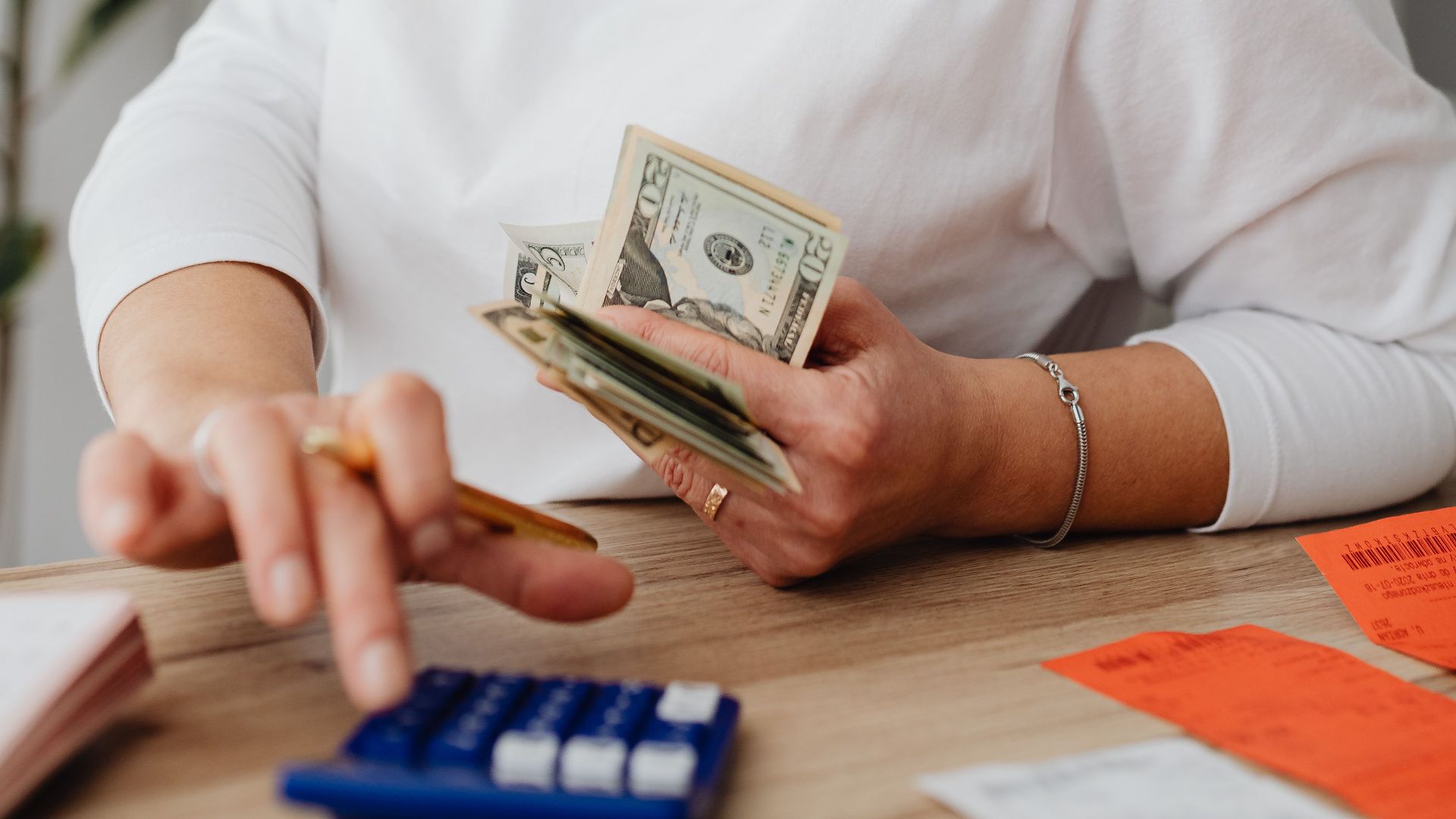 Woman using calculator and handling cash for financial planning at home.
