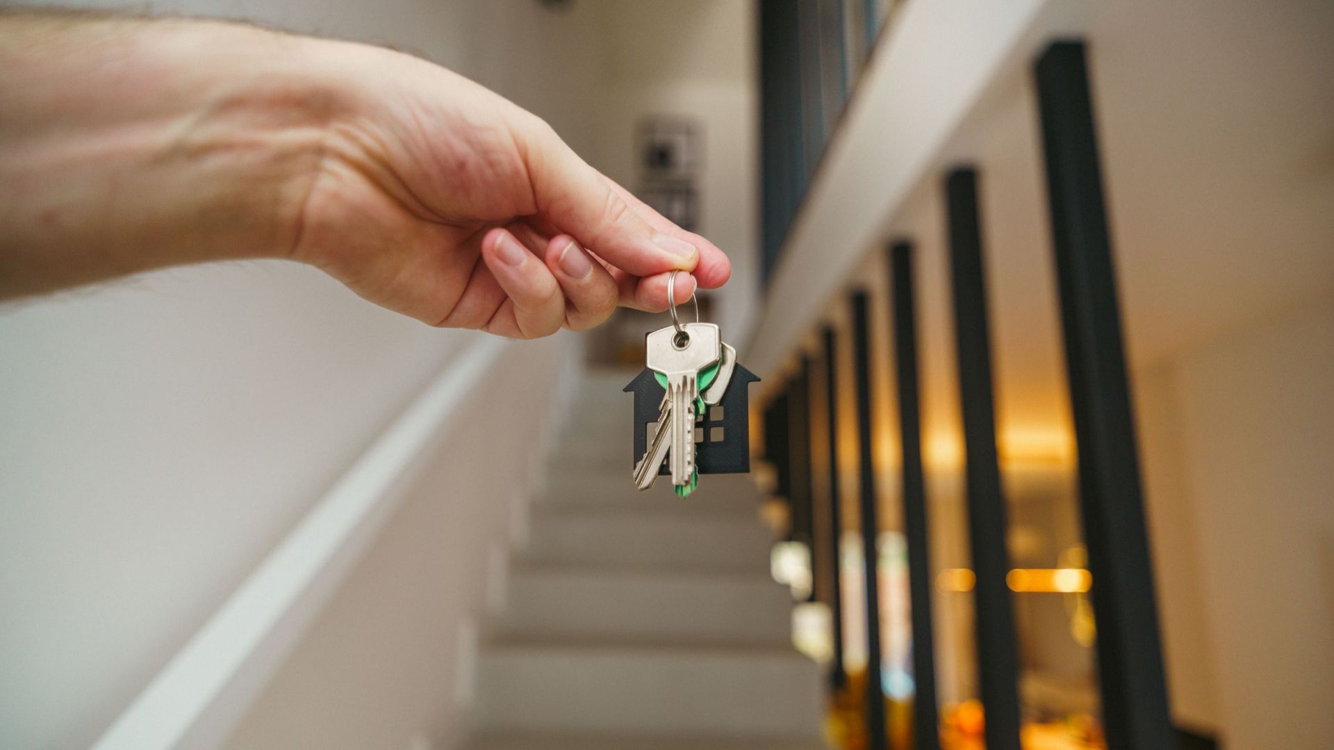 A hand holding house keys in a modern interior, symbolizing new home ownership or real estate investment.