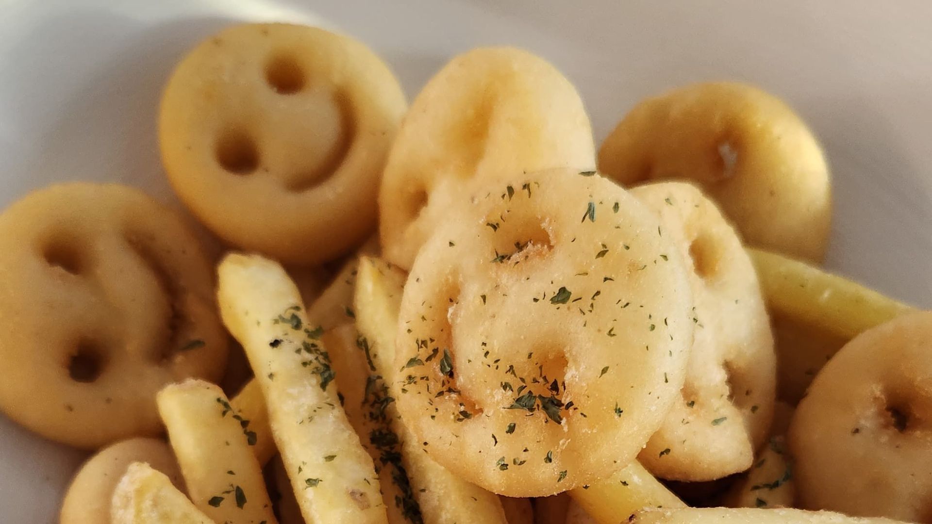 Crispy smiley face potato fries served on a white plate, sprinkled with herbs.