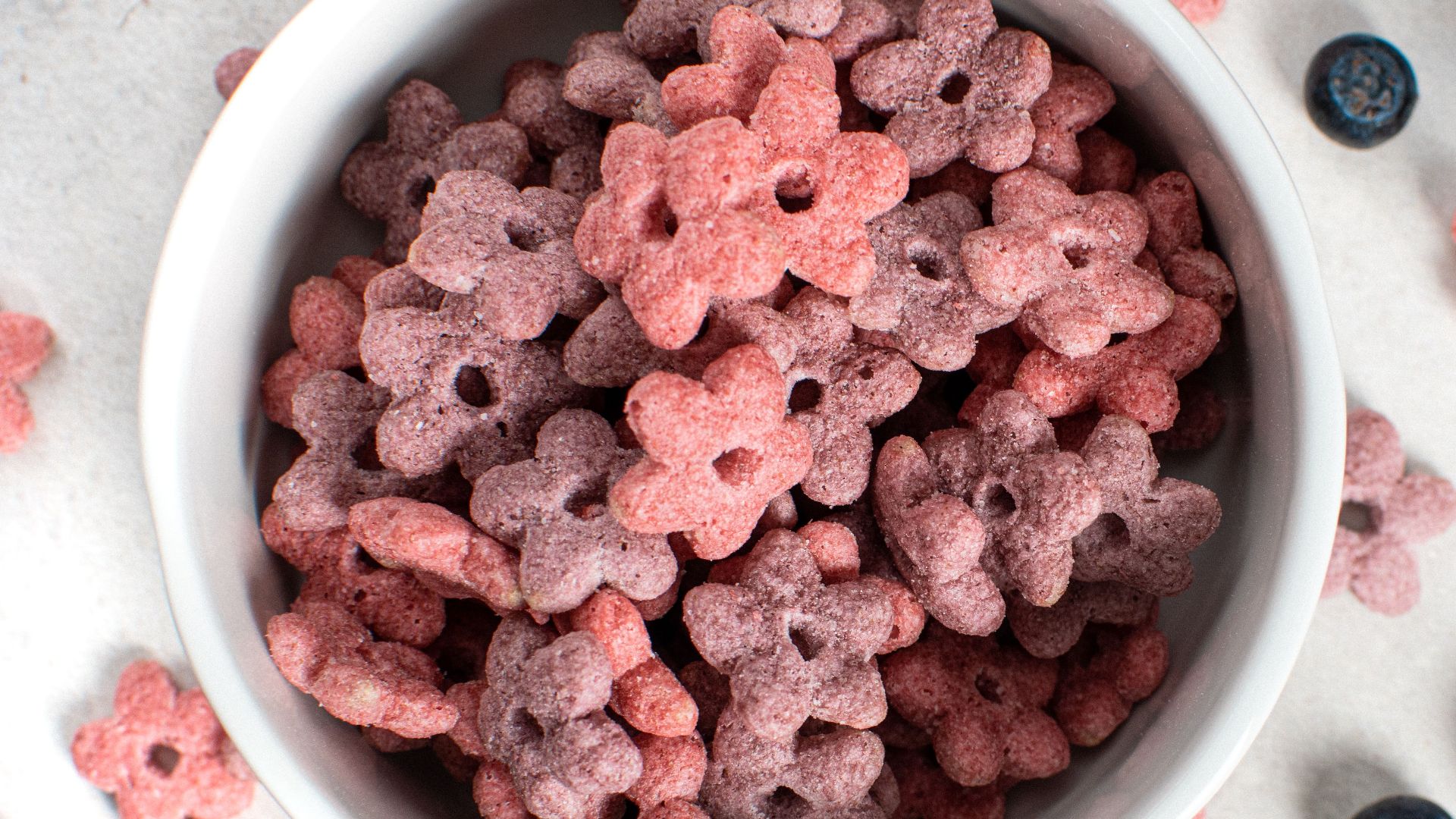 Bowl of berry-shaped cereal with blueberries on a light background.