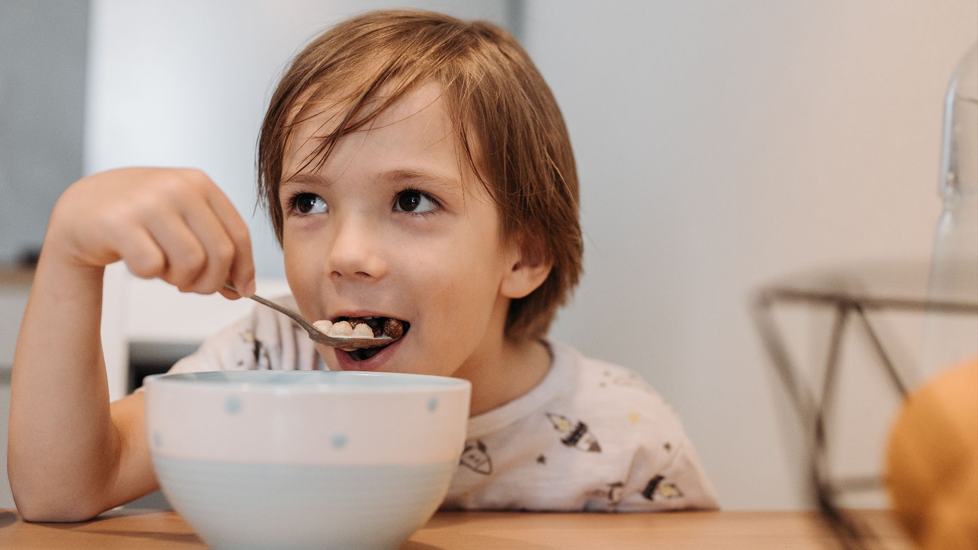 Adorable child enjoying cereal at breakfast indoors with a spoon.