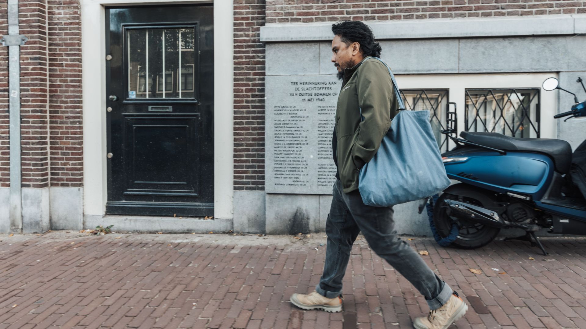 Casual urban scene of a man walking with a blue bag along a brick sidewalk.