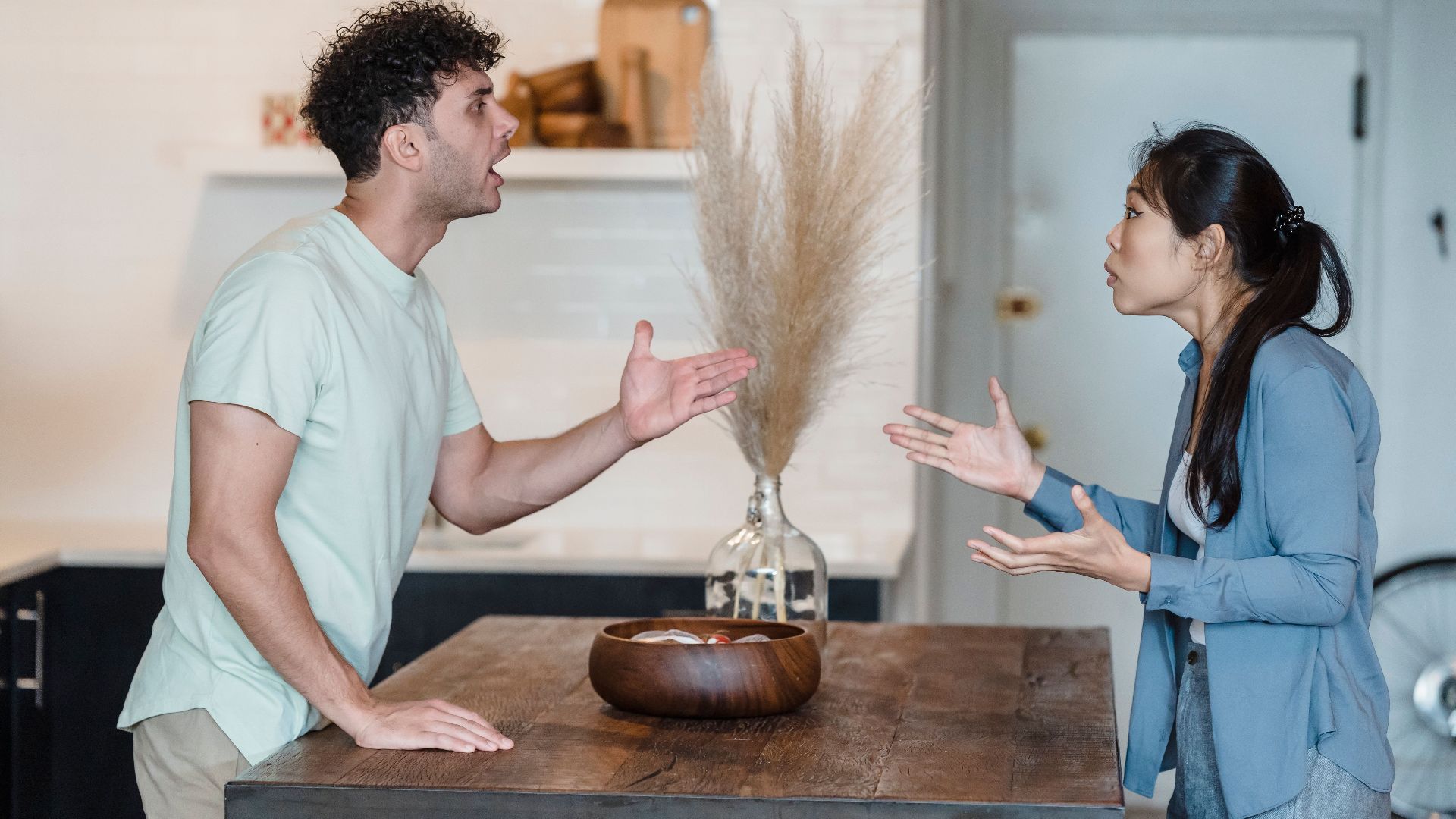 A couple engages in a heated argument at a wooden table in a modern indoor setting.