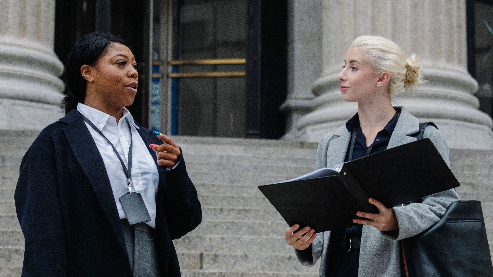 Smart young multiracial female lawyers talking about case standing near aged court building with columns before trial