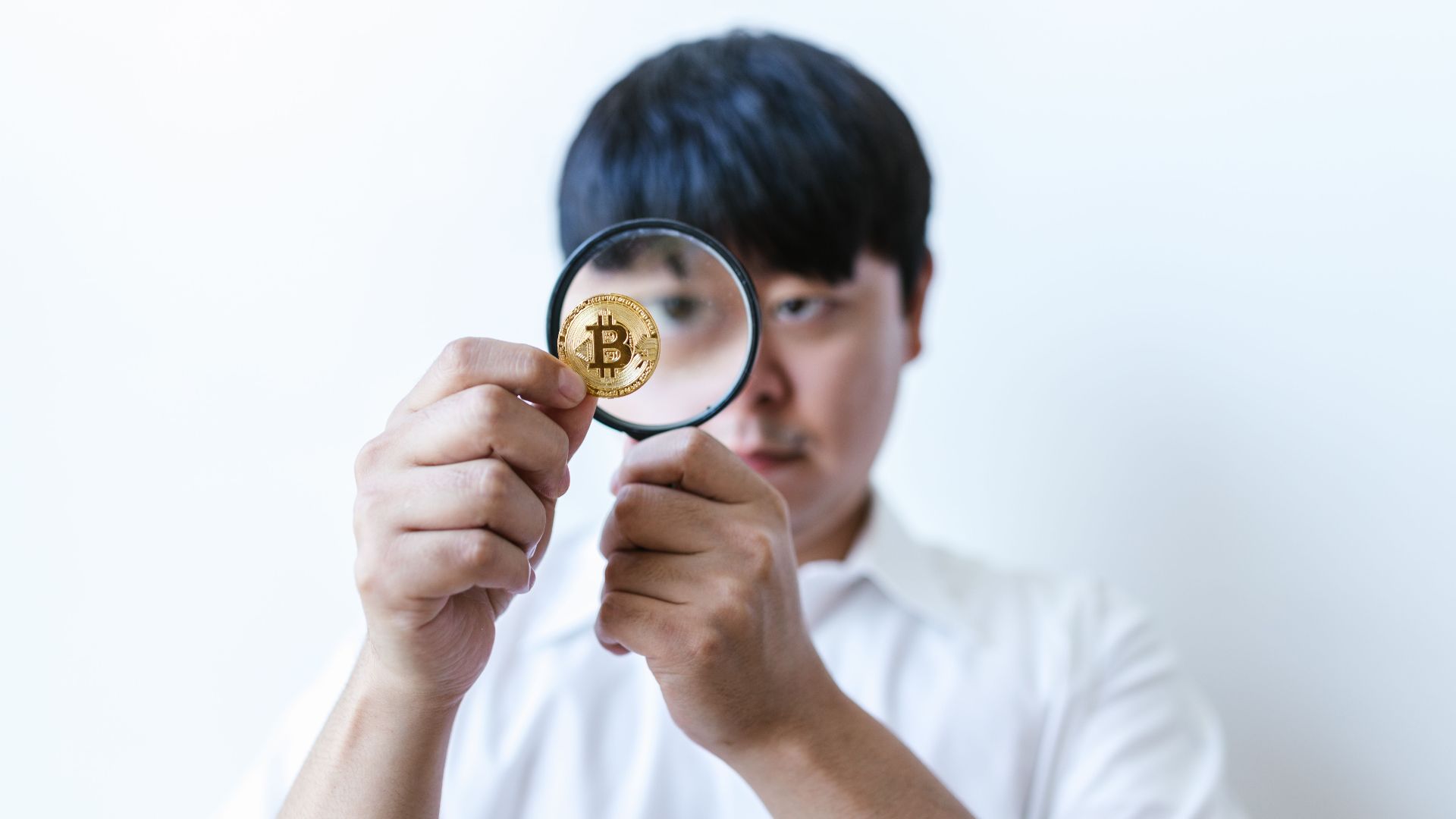 Close-up of a man examining a Bitcoin coin with a magnifying glass, symbolizing cryptocurrency analysis.