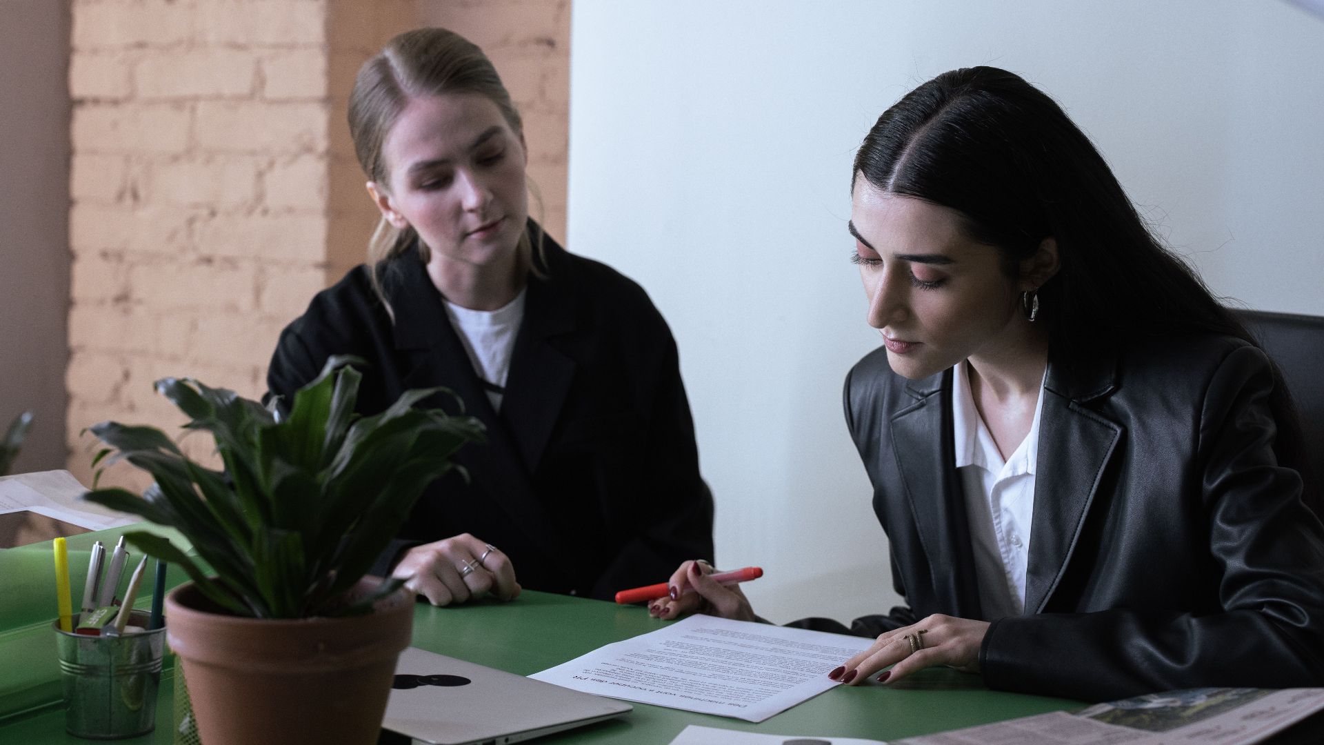 Two women collaborate in a modern office, reviewing documents at a desk.