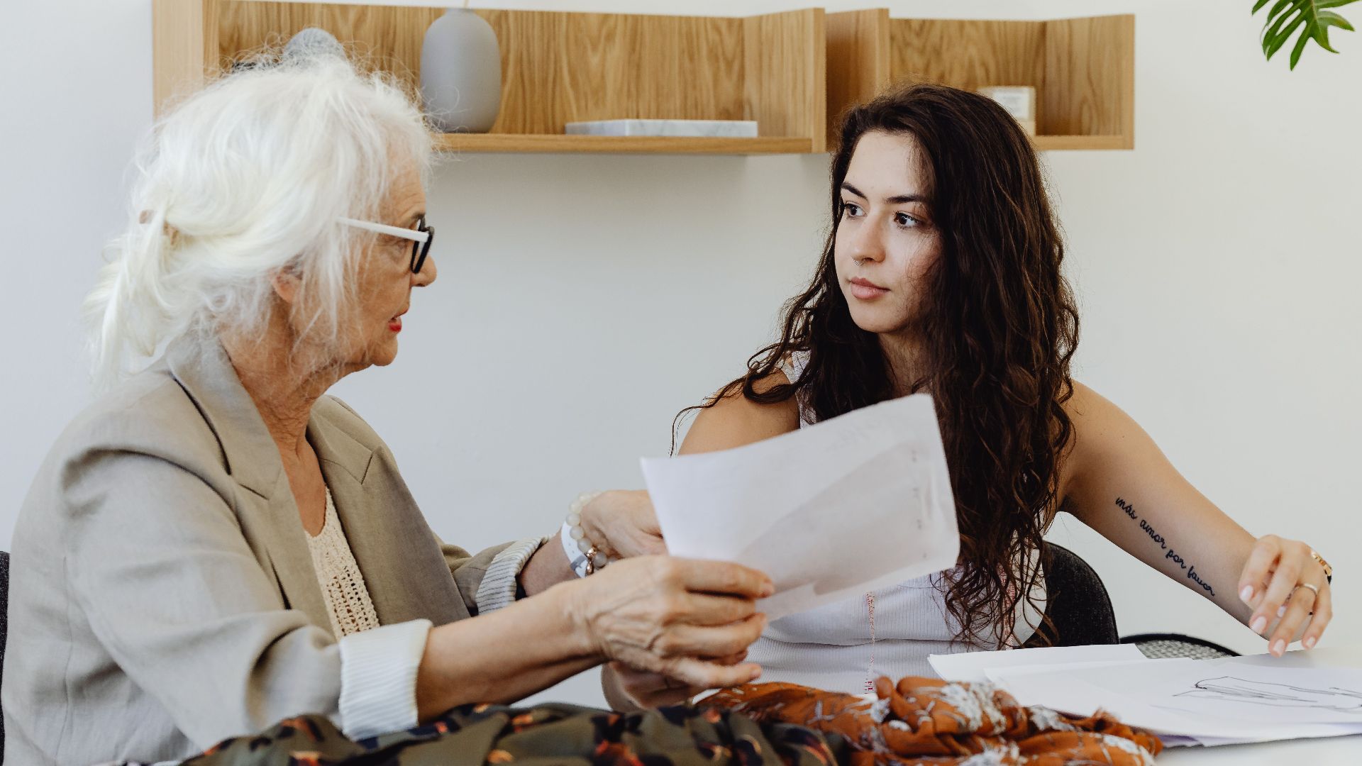 Elderly woman and young woman discussing fabric designs in a fashion meeting.