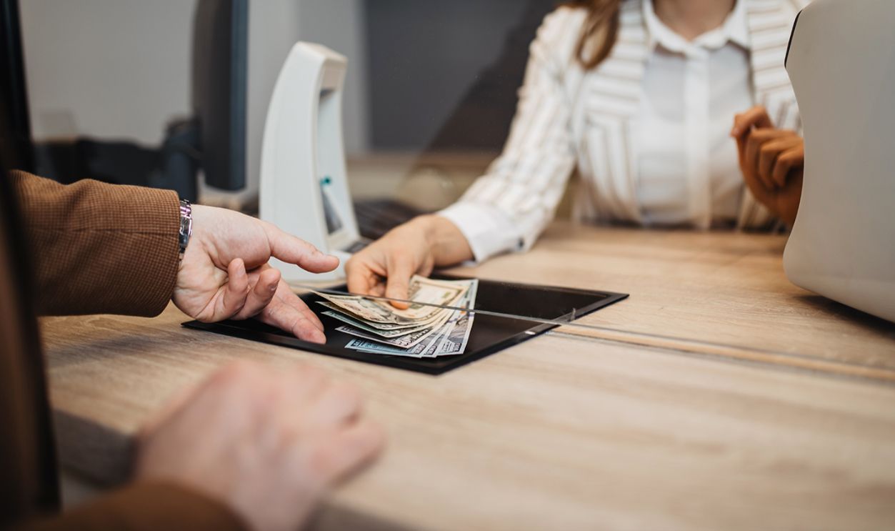 Businesswoman is working in exchange office. She is giving cash money to male customer.