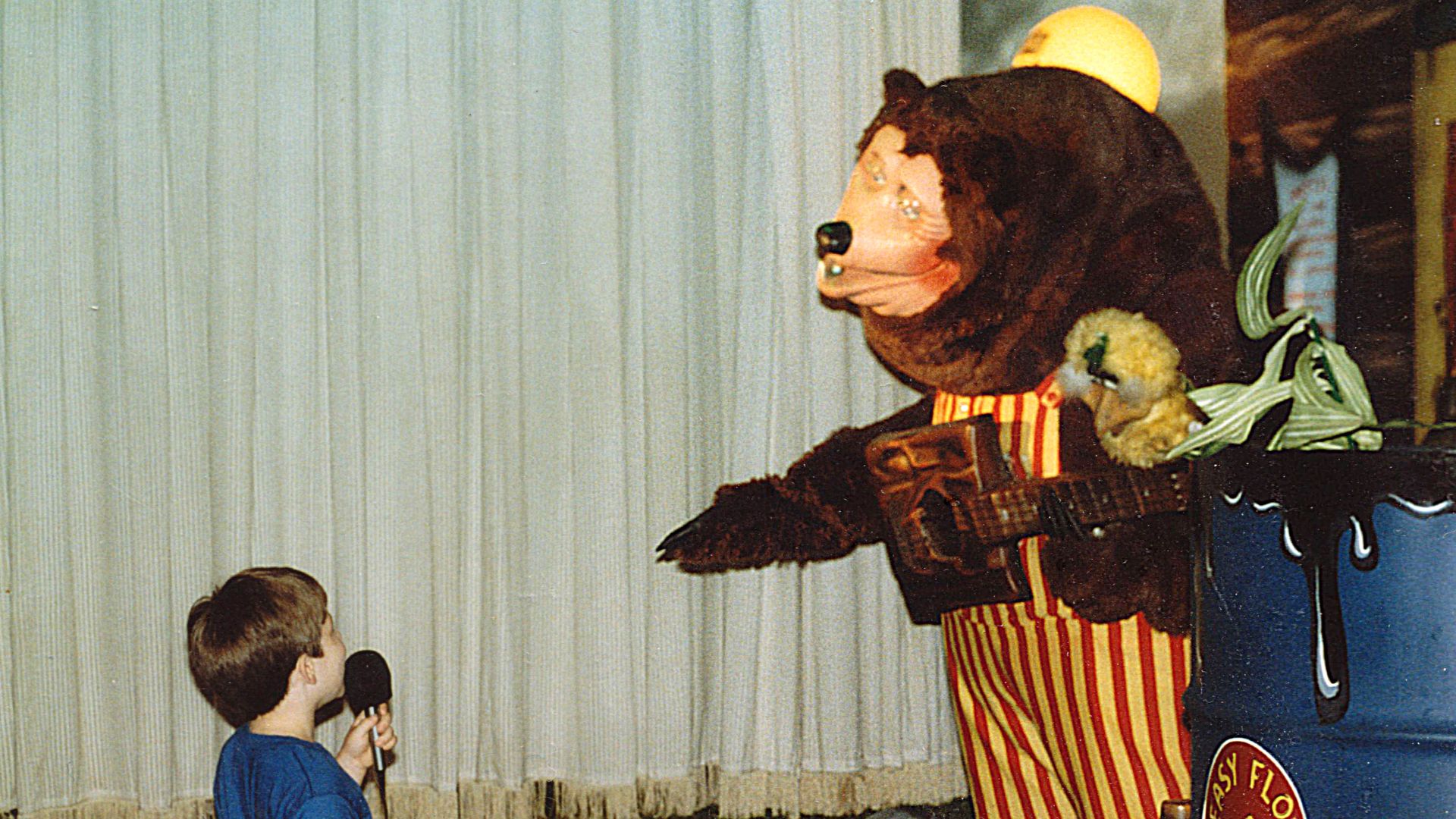 A child uses a microphone to speak to Billy Bob, mascot of ShowBiz Pizza Place, during a birthday party at ShowBiz Pizza in Fayetteville, Arkansas.  The child is Ben Schumin, i.e. User:SchuminWeb.