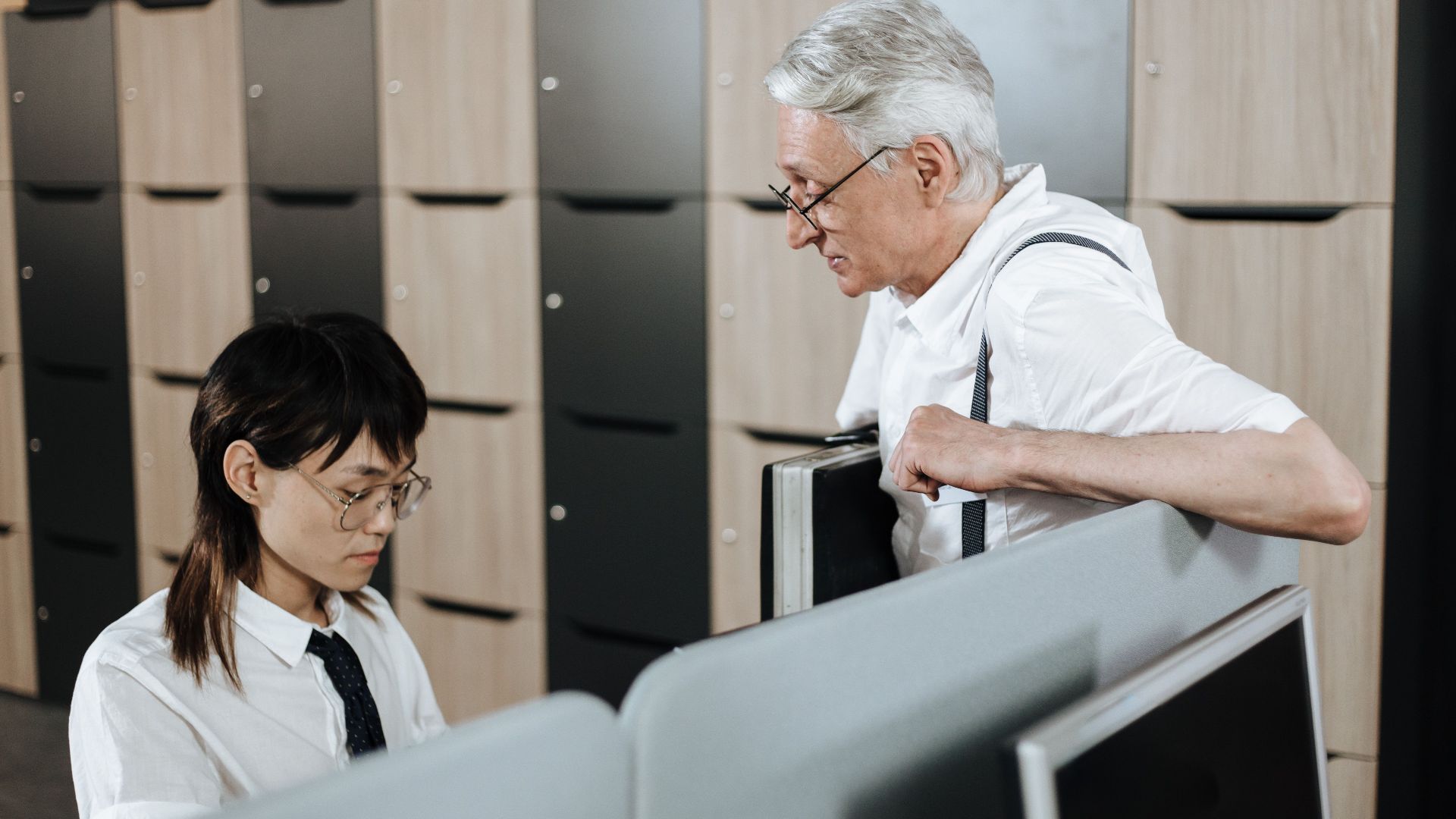 Senior professional engaging with young colleague in an open office setting.