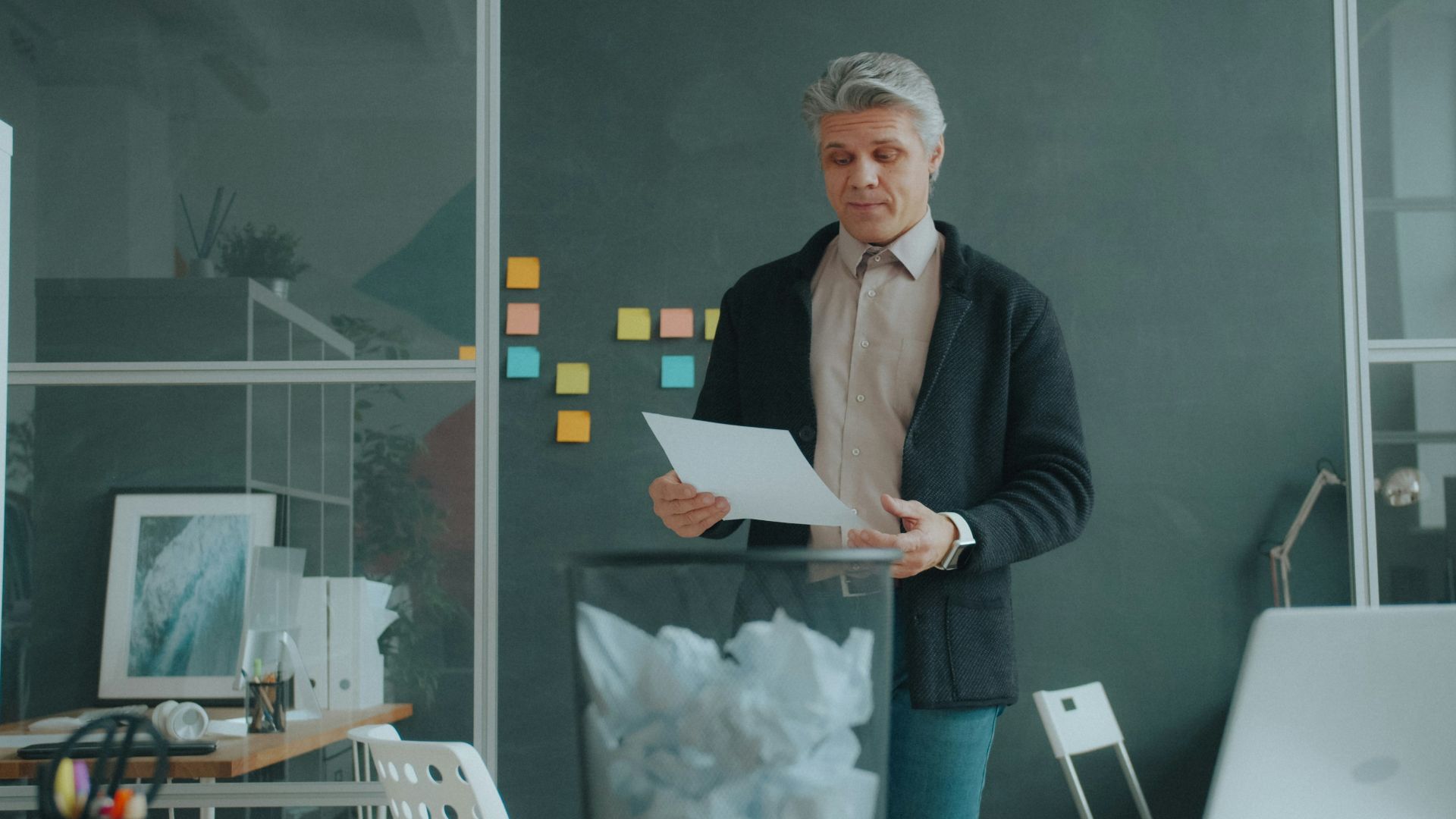 A man holding a document over a wastebasket in a modern office