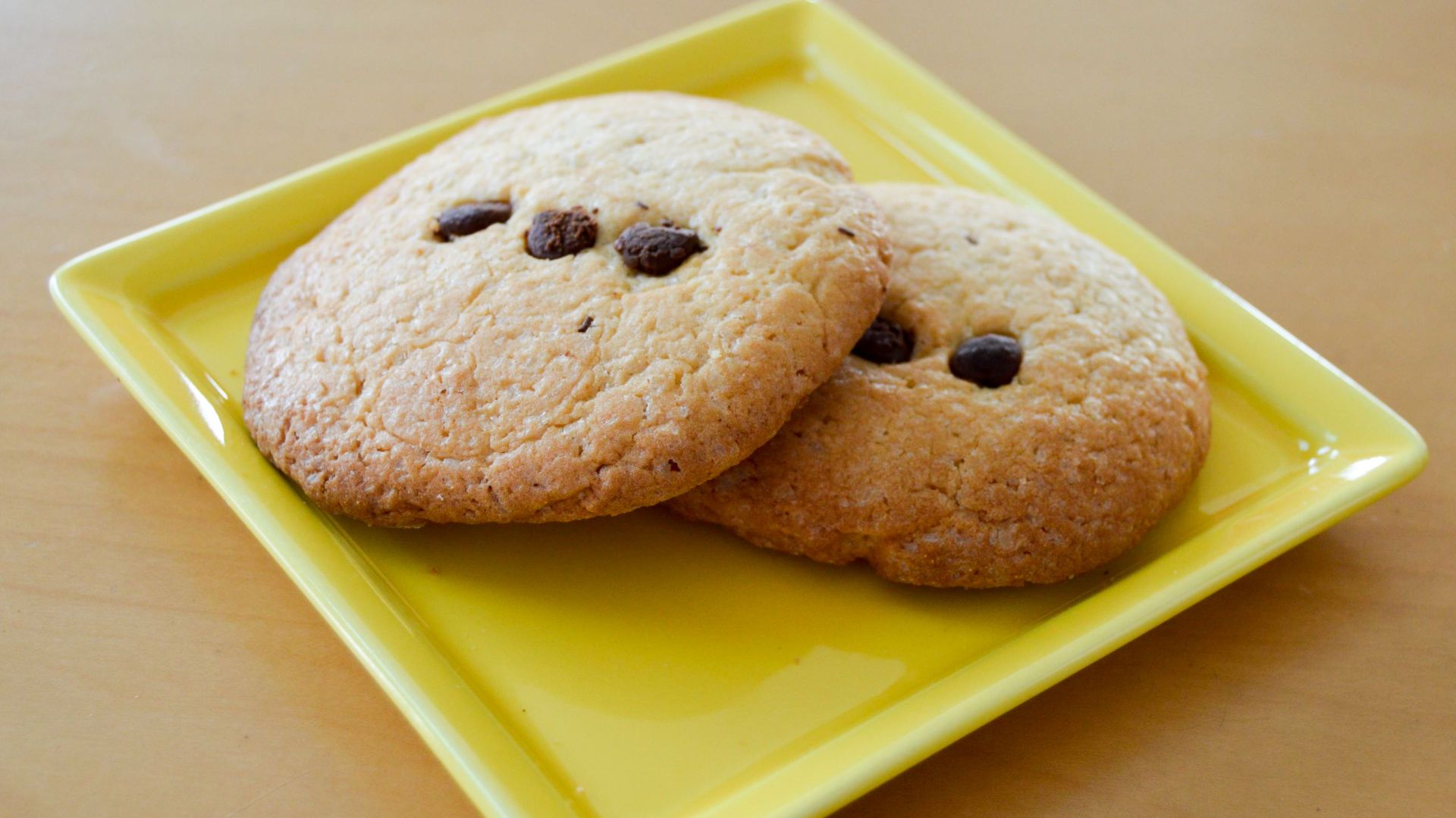 Two freshly baked chocolate chip cookies served on a yellow plate.