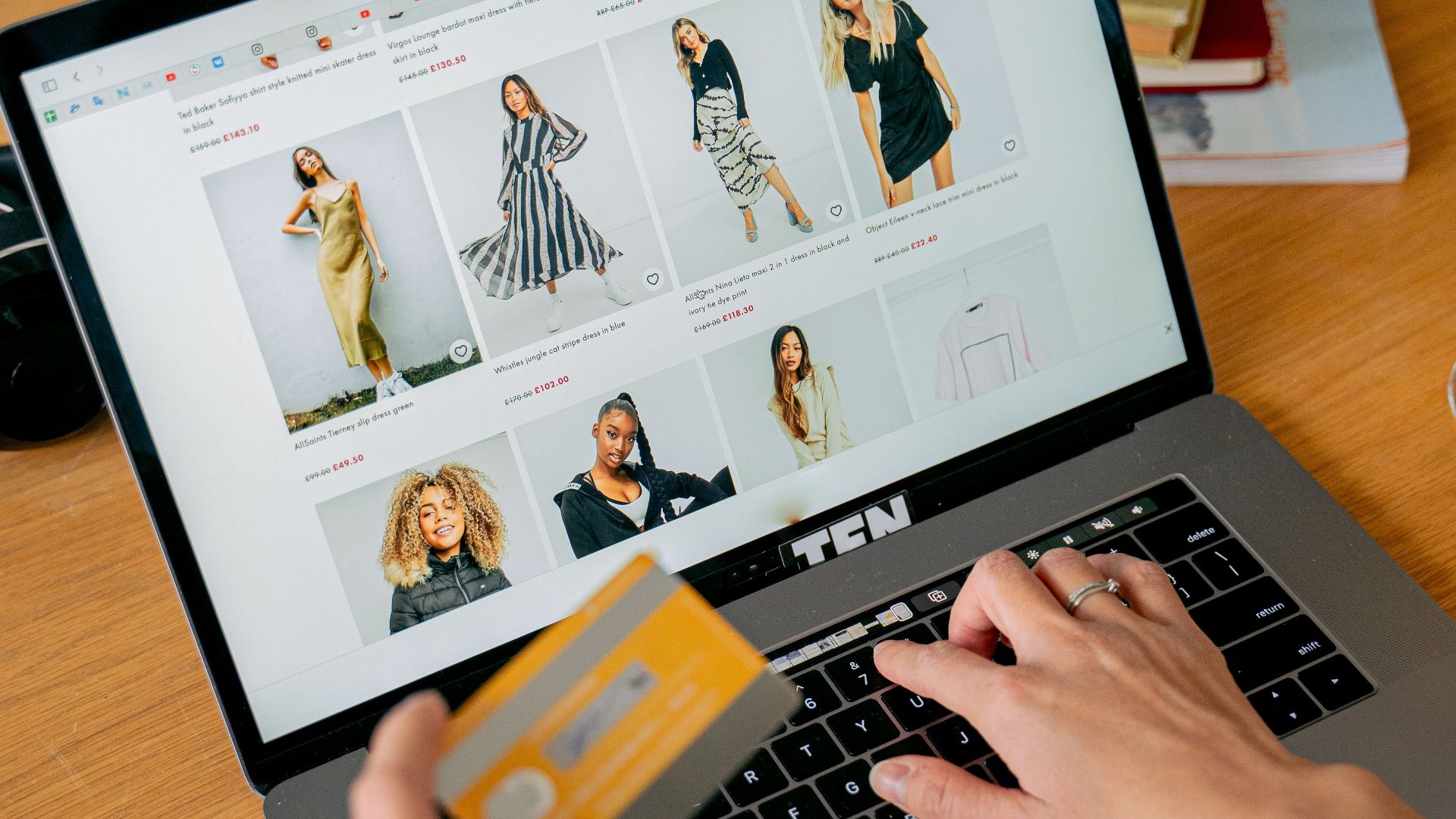 A woman makes an online purchase using a credit card on her laptop, browsing an online fashion store.