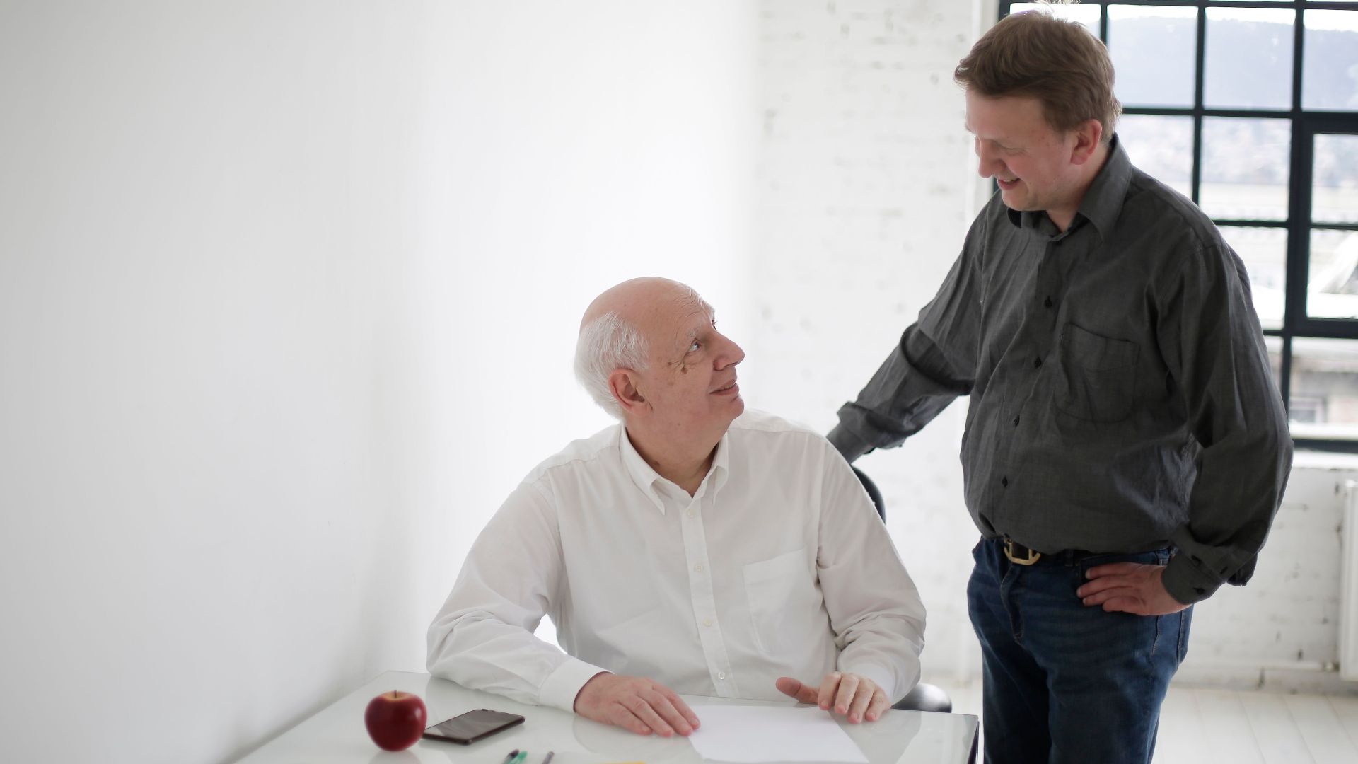Positive men in different ages discussing project while working in loft styled workplace and looking at each other