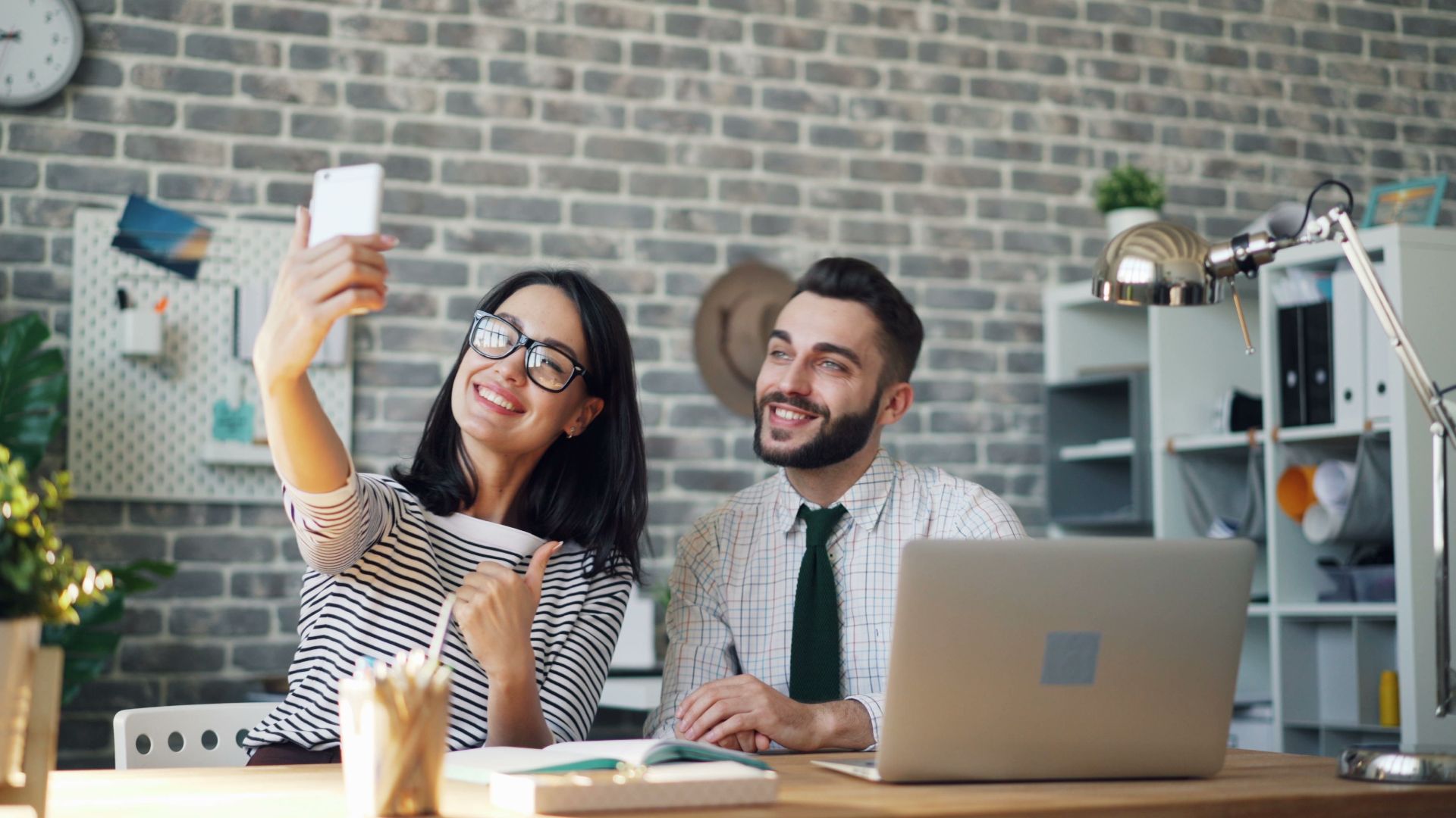 Smiling colleagues capturing a fun selfie moment at their stylish workspace with a smartphone.