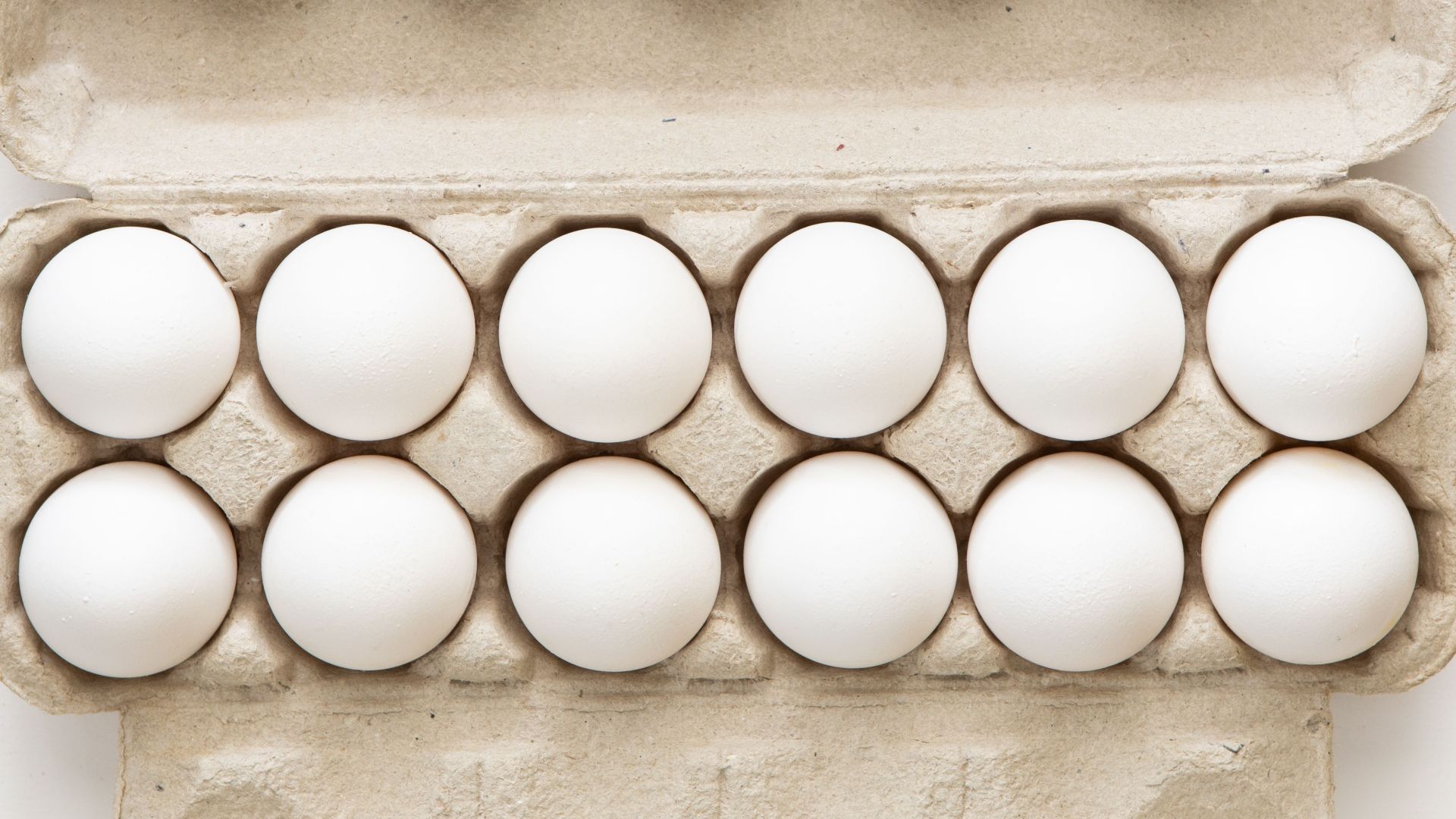 Minimalist flat lay of white eggs in a carton tray, perfect for culinary or health concepts.