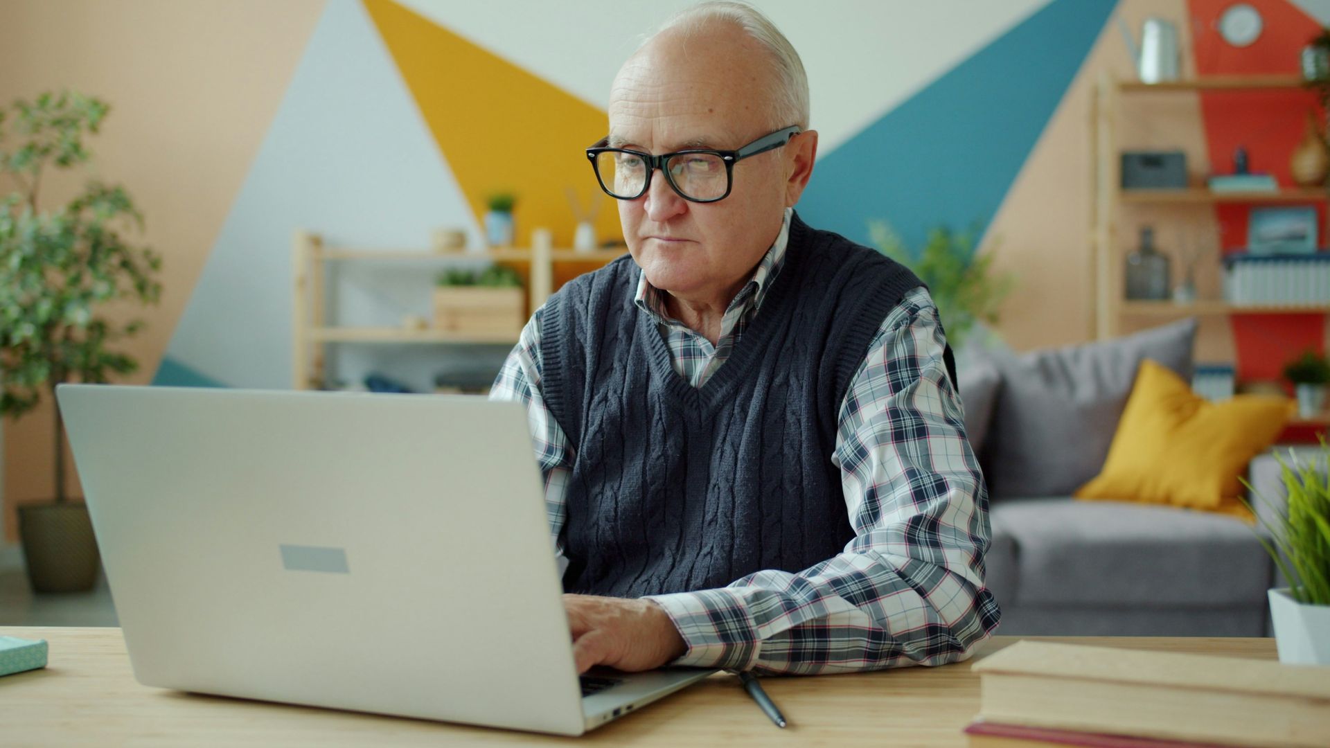 Elderly man wearing glasses using a laptop at home