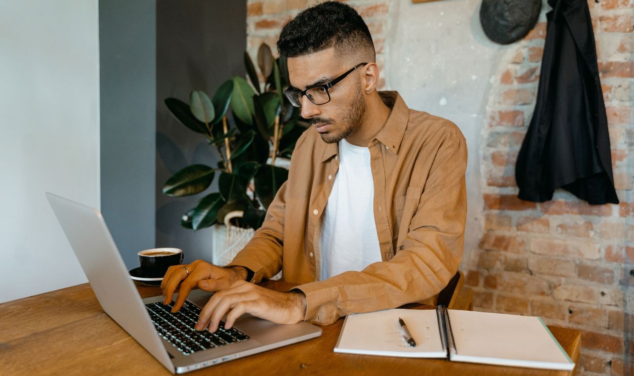 Man in casual office setting typing on laptop with coffee and notebook
