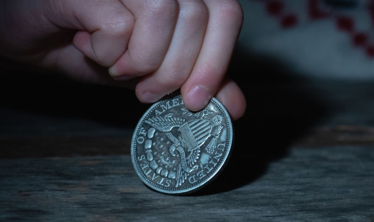 Sad young girl holding coins as symbol of poverty. Horizontal image. Selective focus on hand and coin.
