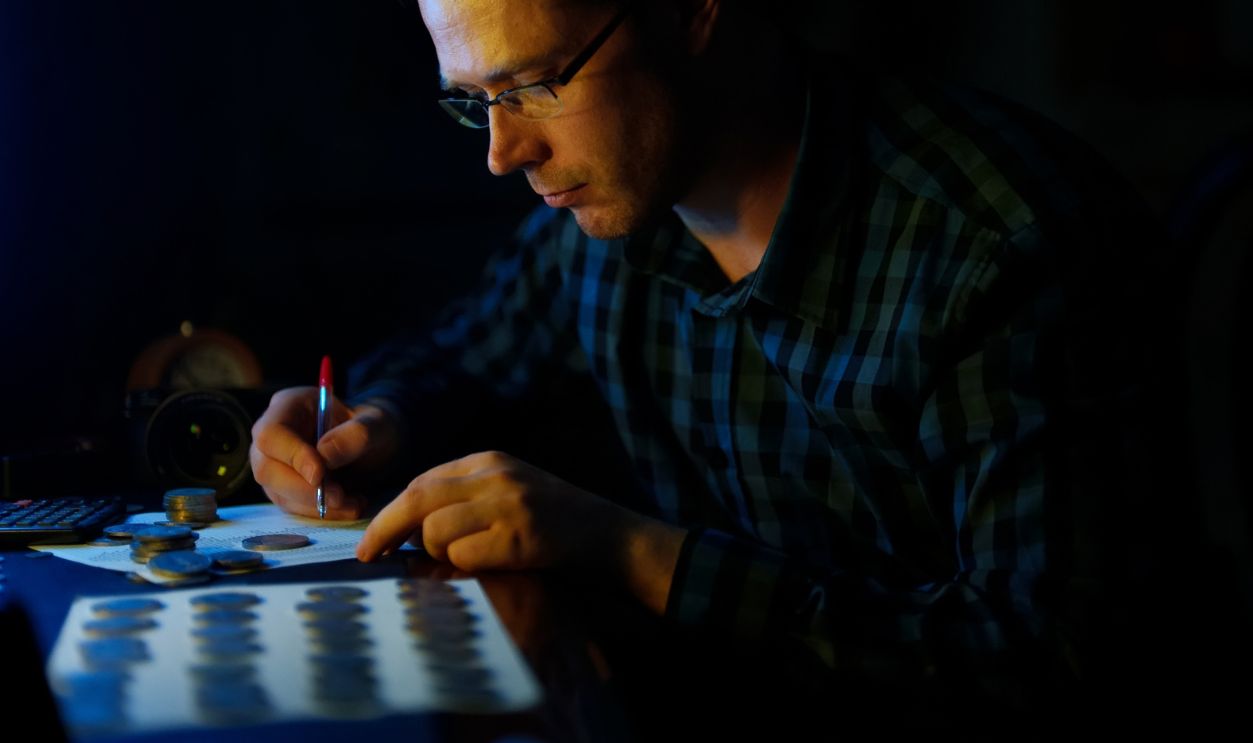 Male numismatist examines collection of coins.