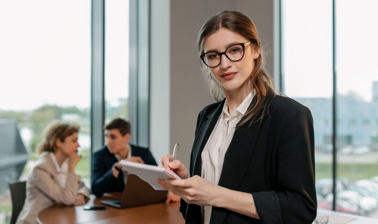 Confident businesswoman holding notebook during meeting in modern office