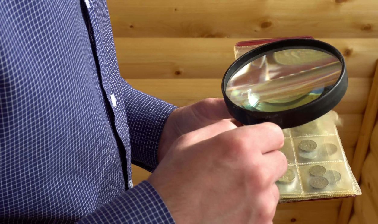 numismatist considers old coins through magnifying glass.