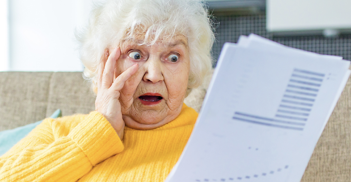 shocked amazed old woman white gray-haired sitting on the sofa in living room with laptop and bills