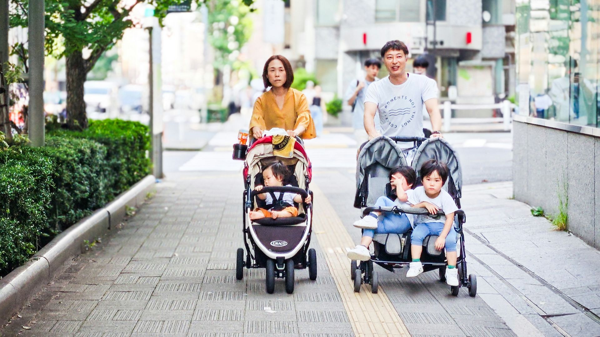 Parents pushing children in strollers on sidewalk