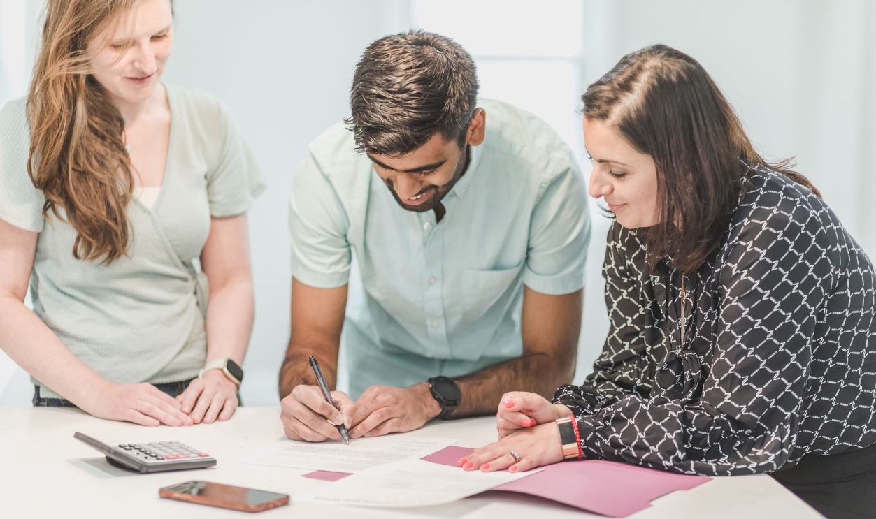 Three adults reviewing and signing real estate documents indoors.