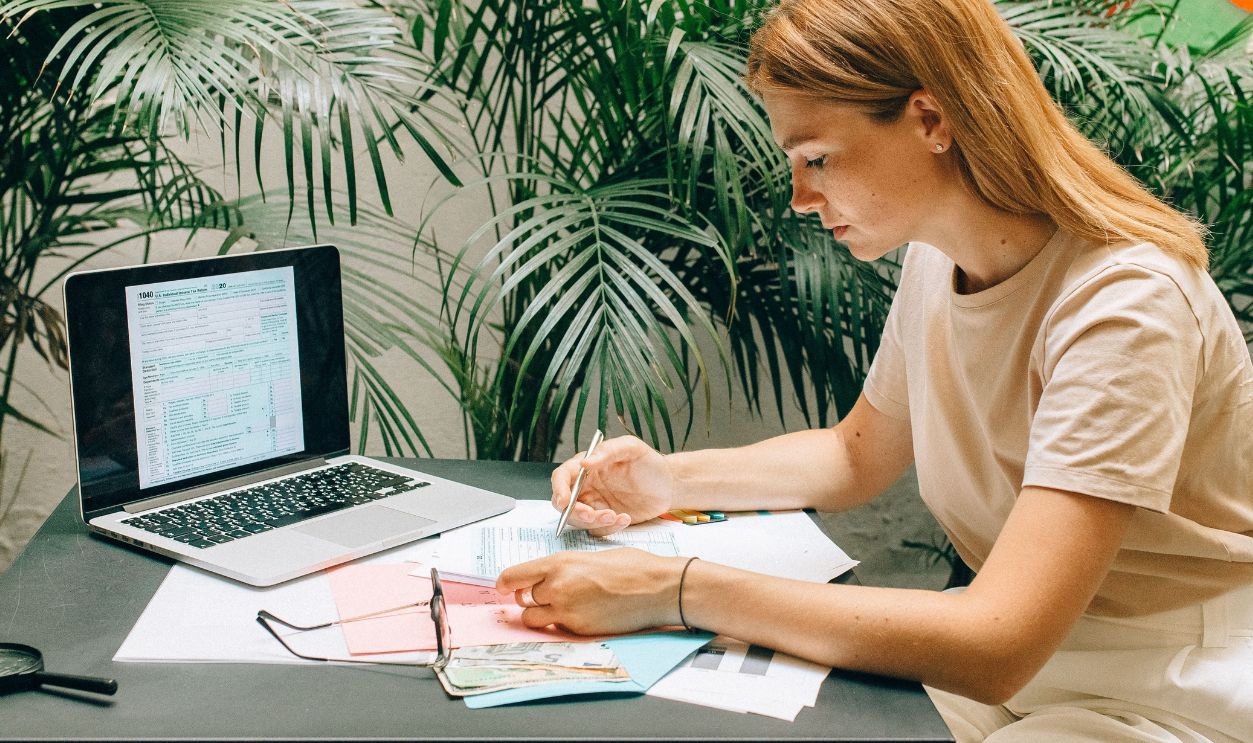 A woman deeply concentrated on work at her laptop amidst indoor greenery and documents