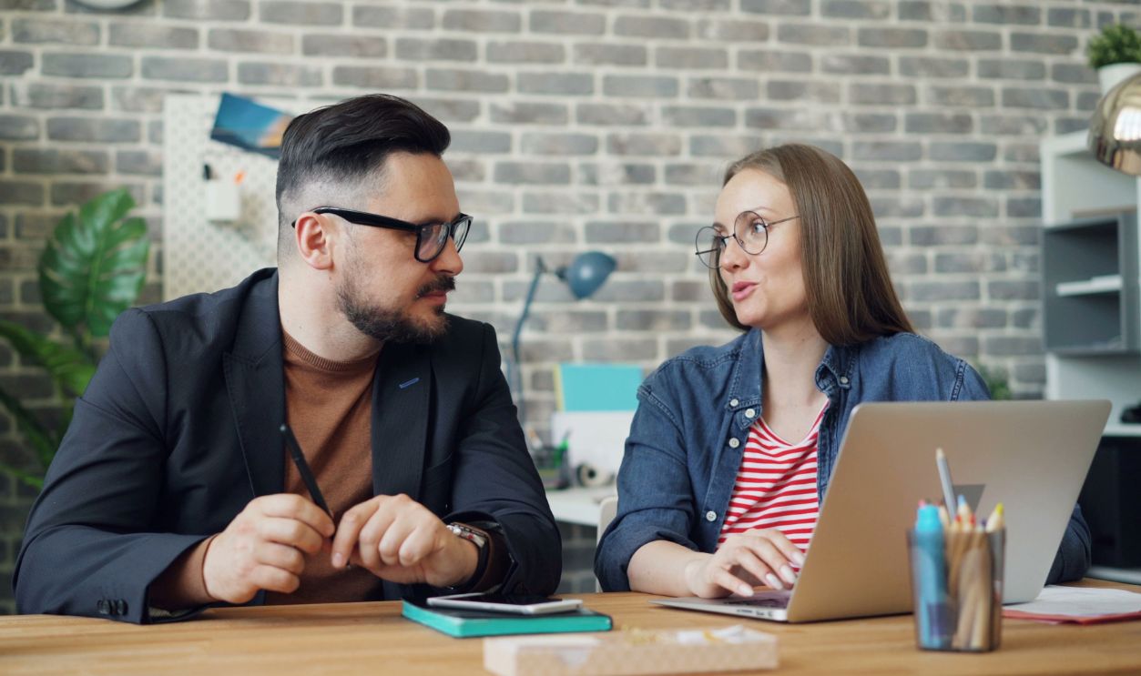 Two colleagues discuss ideas at a desk in a contemporary office