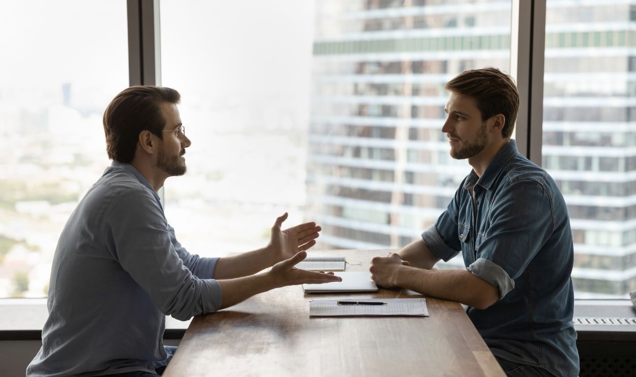 Shutterstock-1997387945, Side view confident young male job seeker talking with skilled hr manager at job interview. Professional lawyer or financial advisor consulting client at business meeting in modern office room.