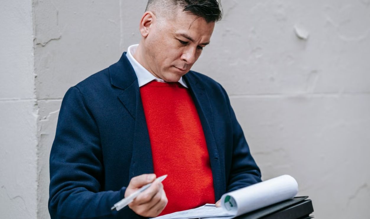 A focused professional man in stylish attire writing notes on paper outside