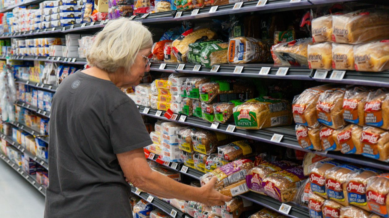 Shutterstock-2817180437, Williston, Vermont, USA - July 21 2026: Elderly shopper examines bags of sliced bread in an aisle in the grocery store