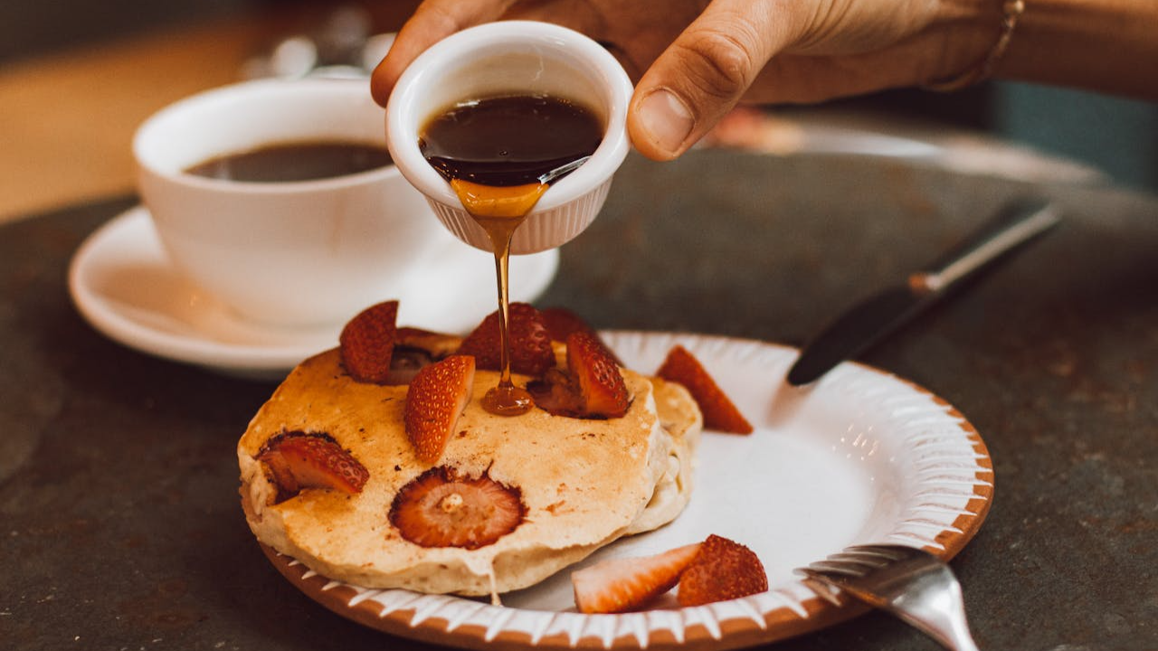 Pouring maple syrup on Pancakes with Strawberries