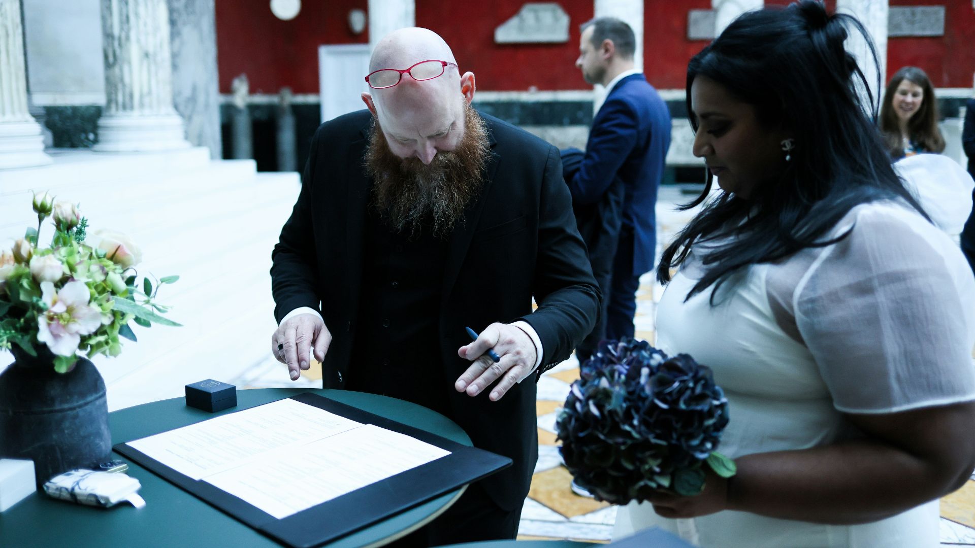 Couple signing wedding papers with guests watching