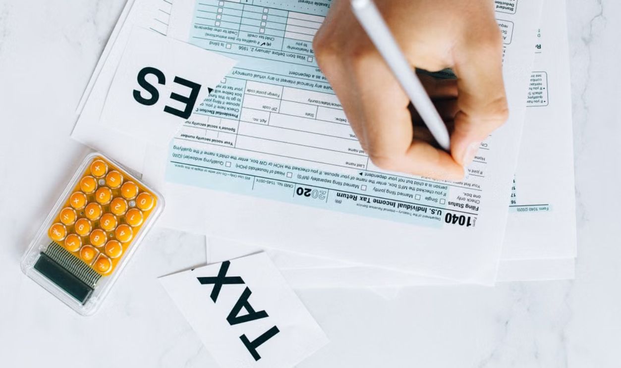 Close-up of hand writing on tax form with calculator nearby on white surface