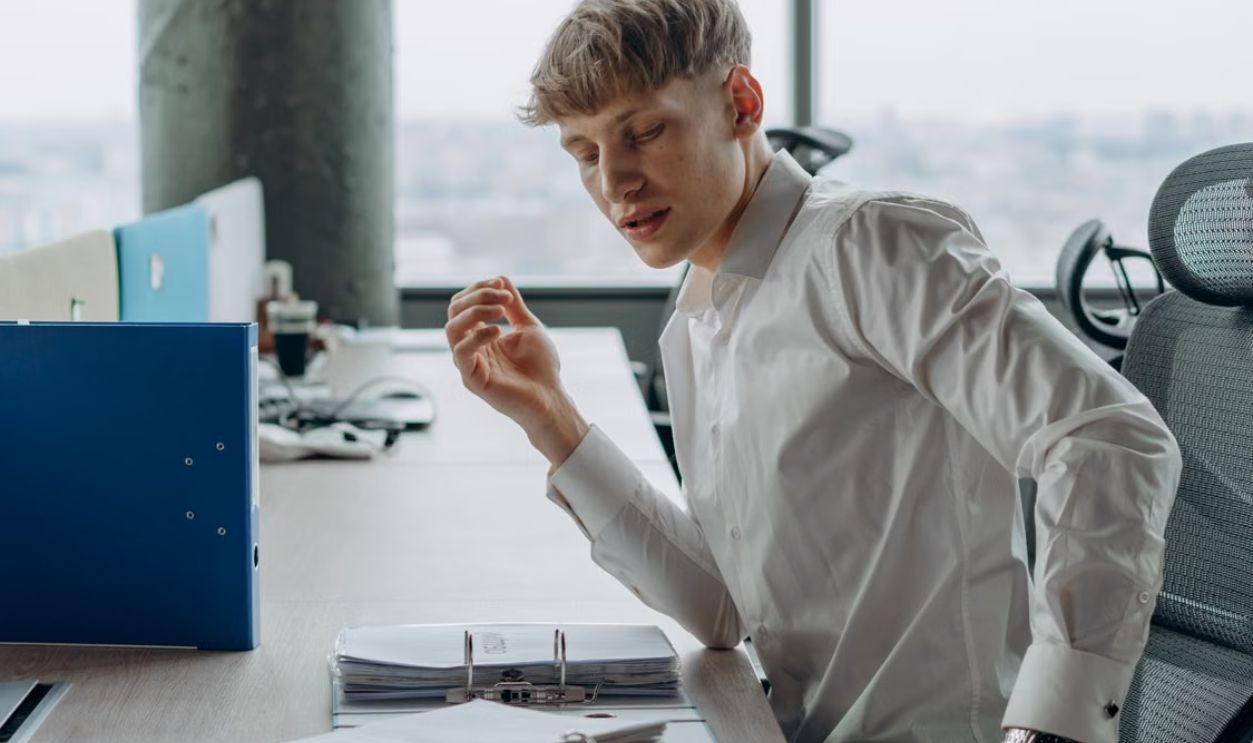 Man in white shirt sitting at office desk reading documents, modern workspace