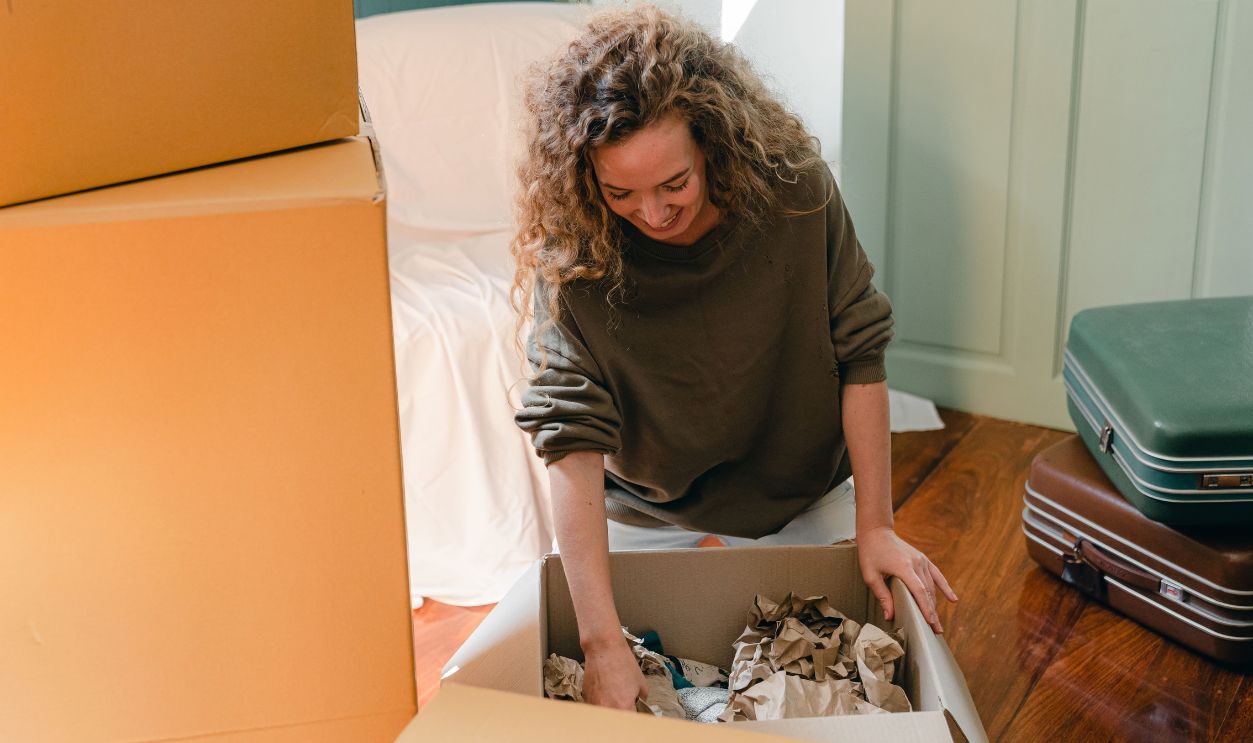 A cheerful young woman unpacking boxes in her new home, feeling content
