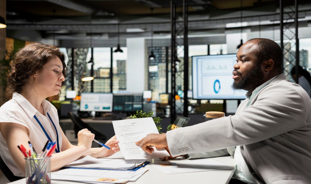 HR manager and job seeker discuss personal and professional benefits package such as salary, rights and other onboarding terms. Reviewing CV and contract document in a corporate setting.