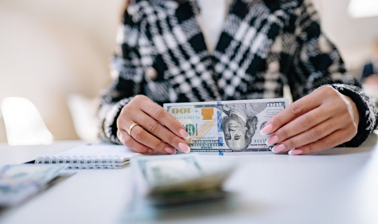Close-up image of hands holding a US hundred dollar bill on a desk