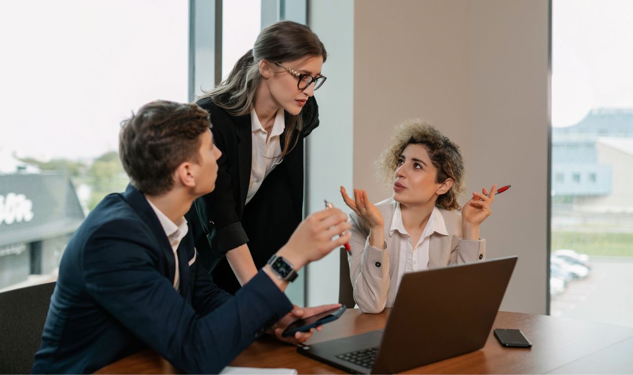 Three professionals in a business meeting, discussing work around a laptop