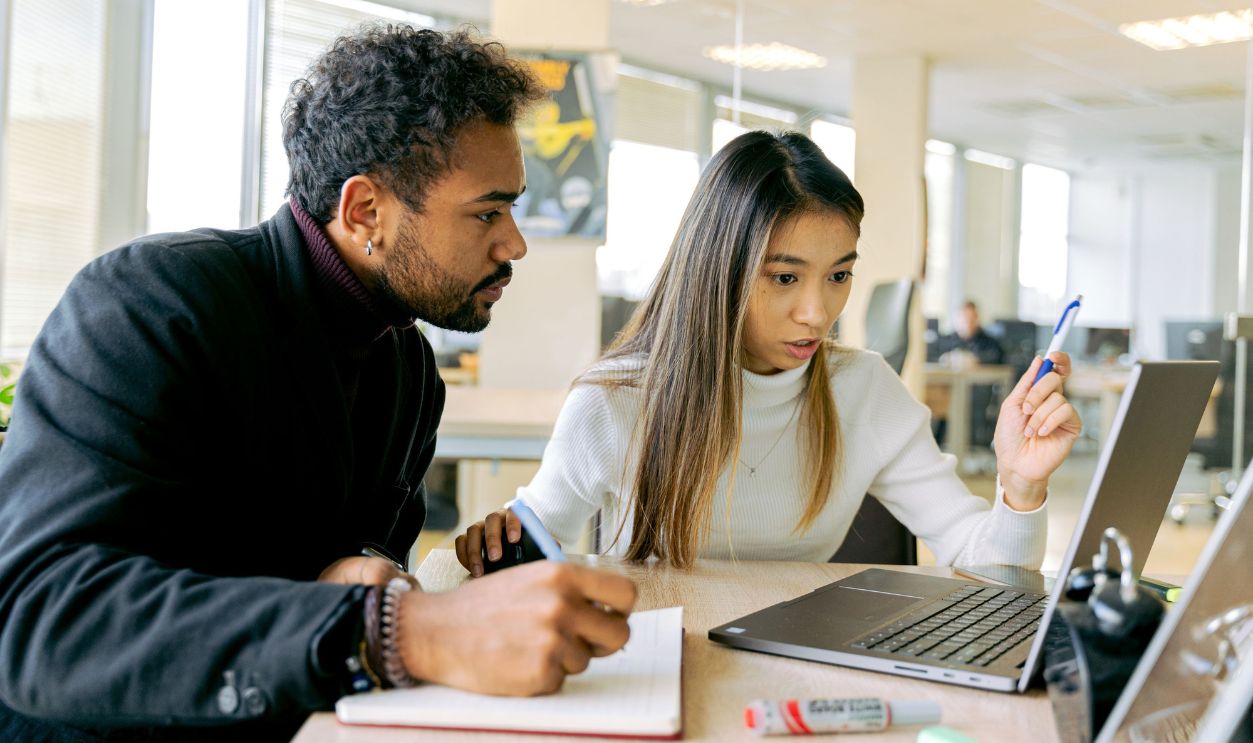 Two young professionals discussing work at a laptop in a contemporary office
