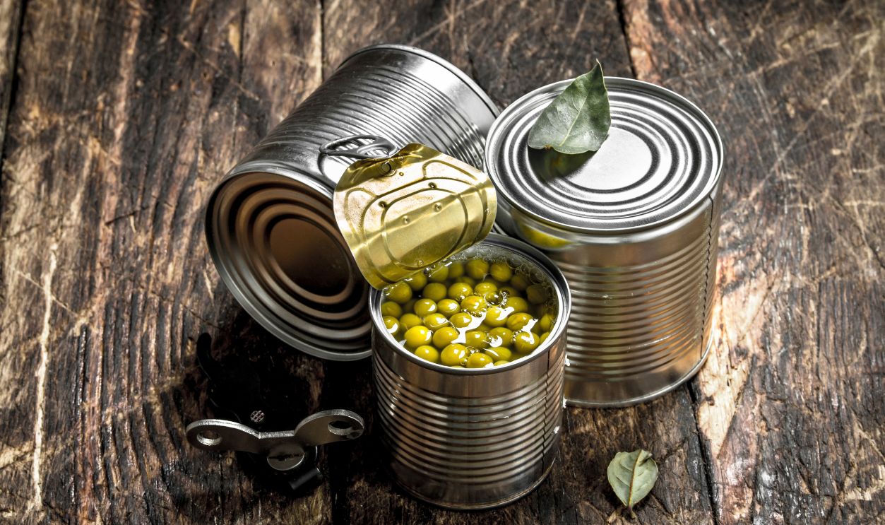 Canned green peas in a tin can with opener. On a wooden background.