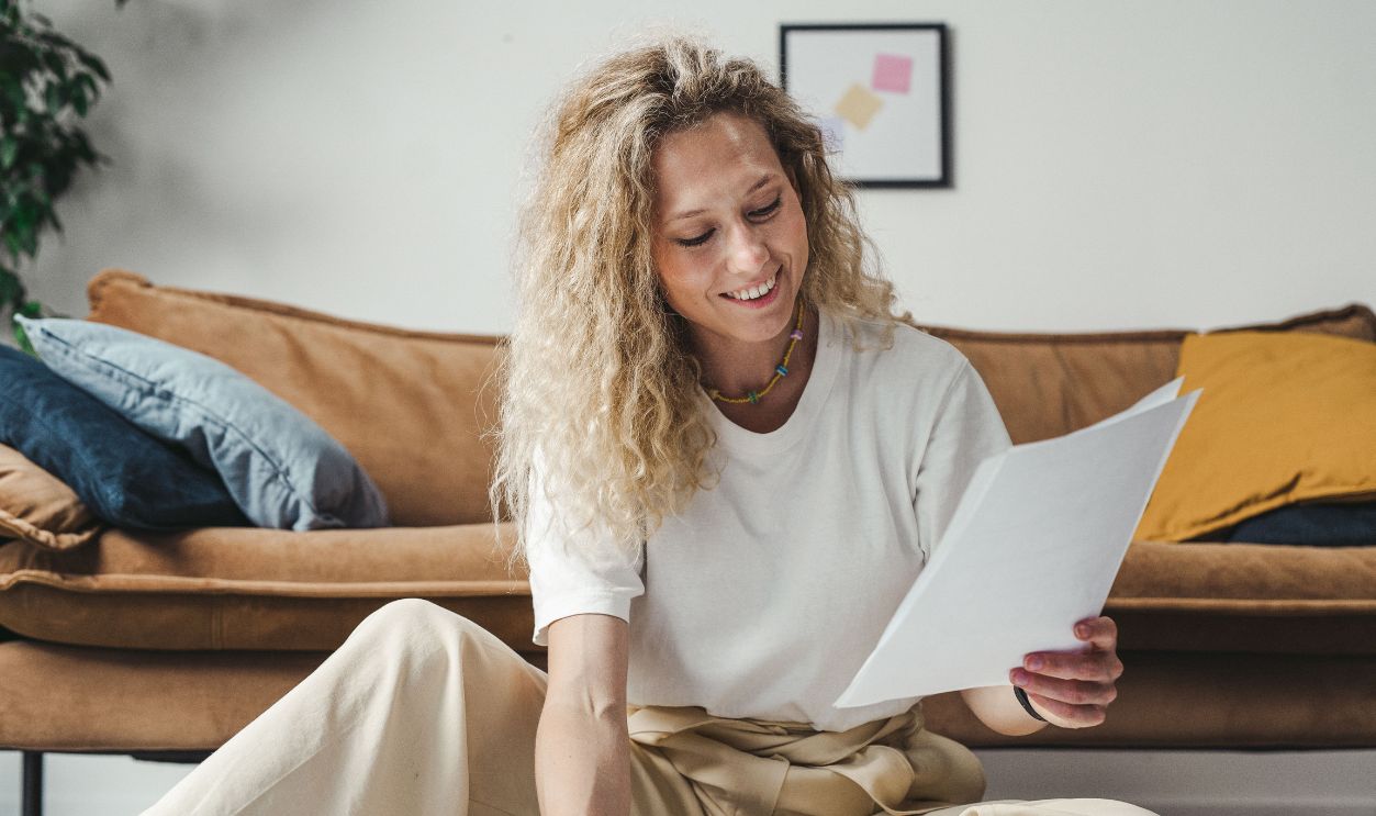 Woman reviewing papers on the floor in modern living room, relaxed and smiling.